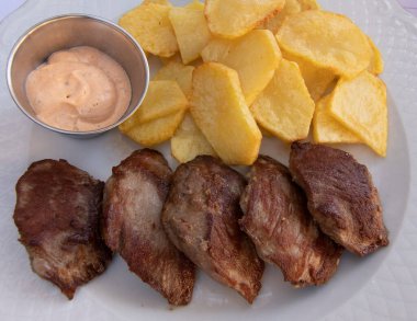 Kızarmış patatesli ızgara sığır filetosu, hepsi beyaz tabakta. Acı soslu bir kase. İspanyol gıda konsepti.