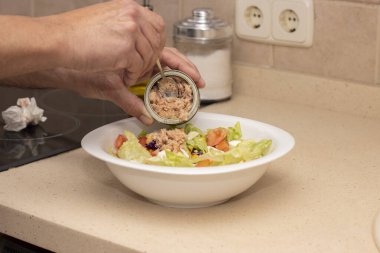 Bir adamın eli karışık salatanın üstüne ton balığı konservesi döküyor. Seçici odak.