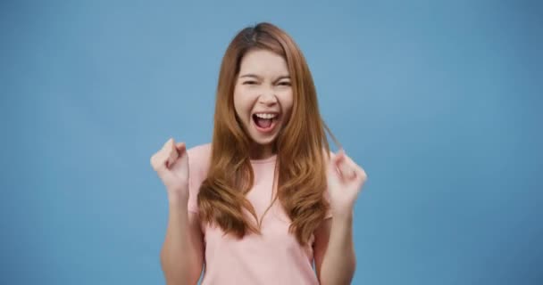 年轻的亚洲女士 有着积极的表情 快乐而兴奋 穿着休闲装 在蓝色的背景下看着相机 快乐可爱的快乐女人为成功感到高兴 面部表达概念 — 图库视频影像