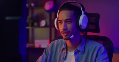 Mutlu Asyalı oyuncu kulaklık takıyor ve gece modern evdeki oturma odasında renkli ışıklı bilgisayar oyunu oynuyor. Esport akış oyunu çevrimiçi, ev karantina etkinliği kavramı.