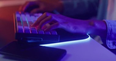 Yakından çekilen eller Asyalı oyuncuyu vurdu. Klavye kullandı ve fare kontrolörü evdeki masada neon ışıklı bilgisayarla oyun oynadı. Çevrimiçi esport çevrimiçi yayın oyunu, ev karantina etkinliği kavramı.