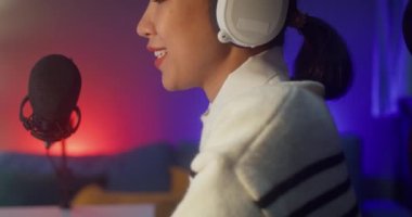 Mutlu Asyalı bayan blogger müzik etkeni bilgisayarda kulaklıklı bir podcast ve oturma odasındaki ev stüdyosunda izleyicilerle mikrofon konuşması kaydediyor. Evde kal, içerik yaratıcısı konsepti.