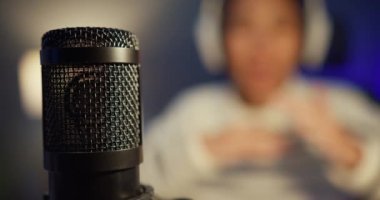 Mutlu Asyalı bayan blogger müzik etkeni bilgisayarda kulaklıklı bir podcast ve oturma odasındaki ev stüdyosunda izleyicilerle mikrofon konuşması kaydediyor. Evde kal, içerik yaratıcısı konsepti.