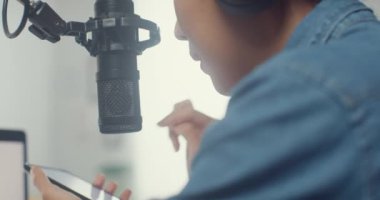 Mutlu Asyalı kız dizüstü bilgisayarda kulaklıklı bir podcast ve oturma odasında izleyicilerle mikrofon konuşması kaydediyor. Kadın podcaster kendi stüdyosundan ses yayını yapıyor. Yakın çekim..