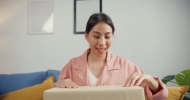 Mutlu Asya 'lı güzel bayan evdeki oturma odasındaki çevrimiçi pazardan karton teslimat paketini açıyor. İnternet üzerinden alışveriş yapan, boks yapmayan, online alışveriş ve dağıtım konsepti olan.