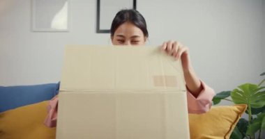 Mutlu Asya 'lı güzel bayan evdeki oturma odasındaki çevrimiçi pazardan karton teslimat paketini açıyor. İnternet üzerinden alışveriş yapan, boks yapmayan, online alışveriş ve dağıtım konsepti olan.