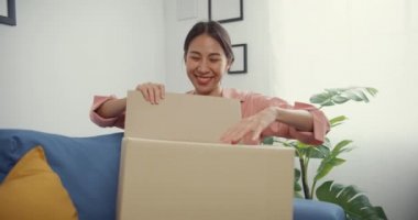 Mutlu Asya 'lı güzel bayan evdeki oturma odasındaki çevrimiçi pazardan karton teslimat paketini açıyor. İnternet üzerinden alışveriş yapan, boks yapmayan, online alışveriş ve dağıtım konsepti olan.