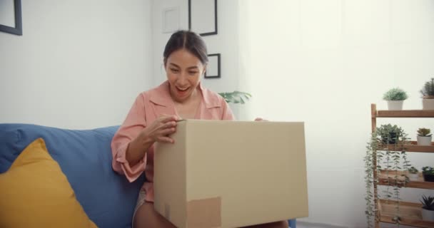美丽动人的亚洲女士在客厅里从网上市场的纸板箱送货包 网上非拳击用品 网上购物和送货概念的满意购物者 — 图库视频影像