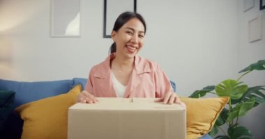 Mutlu Asya 'lı güzel bayan evdeki oturma odasındaki çevrimiçi pazardan karton teslimat paketini açıyor. İnternet üzerinden alışveriş yapan, boks yapmayan, online alışveriş ve dağıtım konsepti olan.