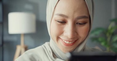 Yakın plan, çekici, Asyalı, genç, neşeli, tesettürlü, tesettürlü güzel bir kadın. Telefonla evdeki rahat oturma odasında online alışverişin tadını çıkar. Kız İslam yaşam tarzı kavramını karantinaya aldı.