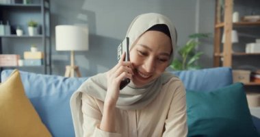 Çekici, neşeli, Asyalı, genç, Müslüman, tesettürlü güzel bir kadın. Evdeki rahat oturma odasında arkadaş ve aileyle gündelik telefon görüşmesi yapıyor. Kız İslam sosyal mesafesi yaşam tarzı kavramını karantinaya aldı.