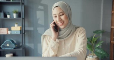 Çekici, neşeli, genç, Asya 'lı, iş kadını, sıradan bir iş kadını, dizüstü bilgisayarla masada oturuyor, telefon görüşmesi yapıyor, iş yerini evdeki iş arkadaşına anlatıyor. Kız İslami yaşam tarzı kavramı.