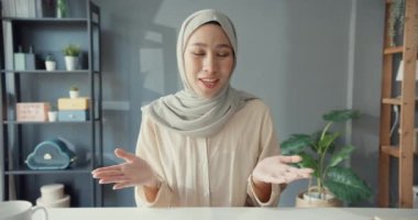 Çekici, neşeli, genç, Asya 'lı Müslüman iş kadını, gündelik olarak masa başında oturuyor ve evdeki oturma odasındaki dizüstü bilgisayardaki uzaktan kumandalı kamera görüntülerine bakıyor. Kız İslami yaşam tarzı kavramı.
