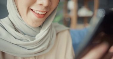 Yakın plan Çekici, genç, Asyalı, İslamcı, tesettürlü güzel kız, gündelik bir şekilde kanepede oturuyor. Telefonu kullan. Başarılı online alışverişin tadını çıkar..
