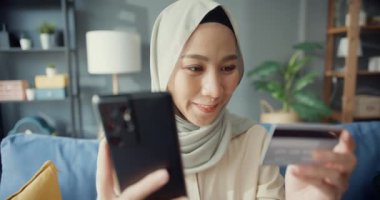 Çekici, neşeli, genç Asyalı, İslami, tesettürlü, tesettürlü, tesettürlü, tesettürlü bir kız. Telefonu kullan. Başarılı online alışverişin tadını çıkar..