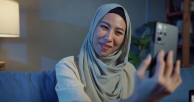 Çekici, neşeli, Asya 'lı Müslüman iş kadını. Kanepede rahat rahat oturuyor. Akşamları arkadaşınla oturma odasında akıllı telefon görüşmeleri yapıyorsun. Kız İslami yaşam tarzı kavramı.
