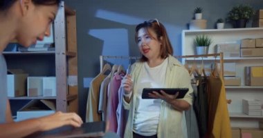 Dizüstü bilgisayara ve tablete gelişigüzel bakan iki Asya 'lı profesyonel genç bayan stok envanter sistemlerini kontrol et siparişi hazırla ve gece müşteriye mal sevkiyatı planla. Yeni iş kurma kavramı.