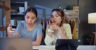 Dizüstü bilgisayara ve tablet toplantısına gelişigüzel bakan iki Asya 'lı genç moda tasarımcısı hisse senedi envanter sistemlerini kontrol edin siparişleri hazırlayın ve gece müşteriye nakliye planları yapın. Küçük işletme kavramı.