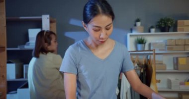 Gündelik stok envanter sistemi olan iki Asya 'lı profesyonel genç bayan geceleri mağazaya gönderilen paketleme siparişi gömlek ürünü hazırlıyor. Yeni küçük işletme kurma kavramı.