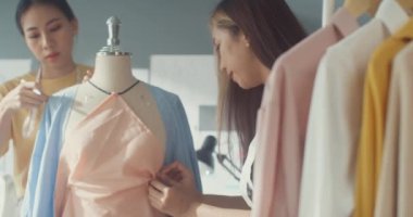 İki profesyonel Asya 'lı neşeli bayan moda tasarımcısı ve dijital tablet mezureli sıradan takım çalışması kuklanın mağazada elbise tasarımı yaratıyor. Yeni bir iş kuran bayan terzi iş ortağı.