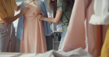 Kumaş paylaşım fikri üzerine gündelik broşlu iki profesyonel Asya moda tasarımcısı bayan takım çalışması kuklanın üzerinde güzel elbiseler oluşturur. Bayan terzi iş ortağı giysi dükkanı açılacak..