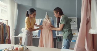 Kumaş paylaşım fikri üzerine gündelik broşlu iki profesyonel Asya moda tasarımcısı bayan takım çalışması kuklanın üzerinde güzel elbiseler oluşturur. Bayan terzi iş ortağı giysi dükkanı açılacak..