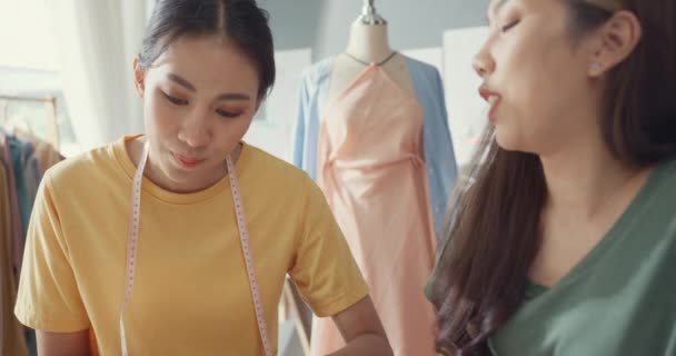 カジュアルなミーティングスケッチブック作品と2つのプロのアジア陽気な女性デザイナーのチームワーク新しいファッションコレクションでは 店内の色の共有のアイデアを議論します レディ テーラーパートナーがビジネスショップを立ち上げる — ストック動画