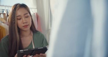Neşeli, profesyonel Asyalı moda tasarımcısı sıradan dijital tabletle dükkanında yeni bir koleksiyon yaratıyor. Bayan terzi çalışma çizimi tablet bloknotu üzerinde Sahte tasarım desenine bakın.