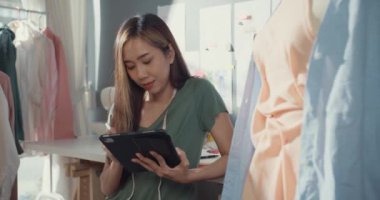 Neşeli, profesyonel Asyalı moda tasarımcısı sıradan dijital tabletle dükkanında yeni bir koleksiyon yaratıyor. Bayan terzi çalışma çizimi tablet bloknotu üzerinde Sahte tasarım desenine bakın.