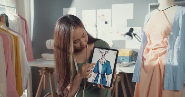 年轻的亚洲女士服装制造商在偶然举行数码平板会议与图形设计师草图讨论样品创建服装设计集合在办公桌上的商店 调整新的创业概念 — 图库视频影像