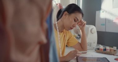Gündelik kullanım tabletine sahip profesyonel Asyalı kadın moda tasarımcısı kafa karıştırıcı düşünce gücüyle yaratıcı ofiste yeni bir koleksiyon yaratıyor. Üniversite atölyesindeki kadın terzi çizimi..