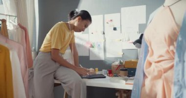 Gündelik kullanım tabletine sahip profesyonel Asyalı kadın moda tasarımcısı kafa karıştırıcı düşünce gücüyle yaratıcı ofiste yeni bir koleksiyon yaratıyor. Üniversite atölyesindeki kadın terzi çizimi..