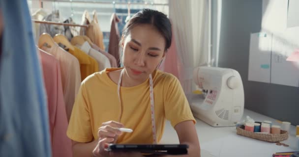 快乐的亚洲职业女性时装设计师 随意使用数码平板电脑 在她的商店里创建新的系列 女士裁缝画草图在平板电脑上看虚拟设计模式 — 图库视频影像