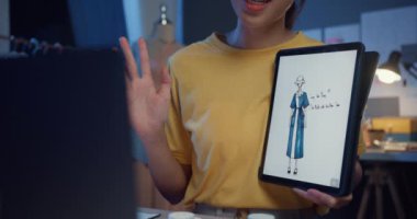 Yakın plan genç Asya bayan terzisi tasarımcı ile dijital tablet toplantı kullanın. Tasarımcı ile tartışın. Örnek elbise tasarımı yeni koleksiyonu geceleyin mağazada masanın üzerinde. Terzi yeni iş kurma kavramı.