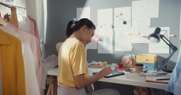 专业的亚洲女性时装设计师带着随意使用数字平板混乱的思维理念 在创意办公室创建了新的系列 大学演播室里女裁缝在平板电脑上画草图 — 图库视频影像