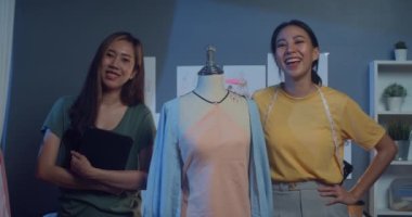 Sıradan dijital tabletli iki profesyonel Asyalı bayan moda tasarımcısı kameraya gece güvenle bakın. Başarılı bayan terzi yeni bir kumaş dükkanı açmaktan gurur duyuyor..