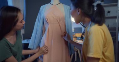 İki profesyonel Asyalı neşeli bayan moda tasarımcısı günlük mesai paylaşımı fikriyle gece kuklası mağazasında güzel elbiseler tasarlıyorlar. Bayan terzi iş ortağı..