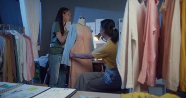 İki profesyonel Asyalı neşeli bayan moda tasarımcısı günlük mesai paylaşımı fikriyle gece kuklası mağazasında güzel elbiseler tasarlıyorlar. Bayan terzi iş ortağı..