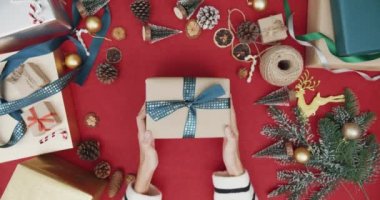 Kırmızı arka planda hediye kutusundan hediye paketini açan kız eli manzarası. Noel kompozisyonu ve yeni yıl tatili sezonunun en az yaratıcı düzlüğü.