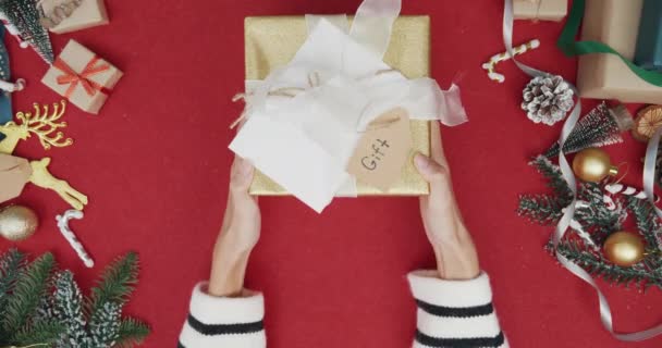 赤い背景に現在のギフトボックスの冬のクリスマスの装飾をアンパック女の子の手のトップビュー クリスマスの伝統的な組成と新年の休日の季節の最小限の創造的なフラットレイアウト — ストック動画
