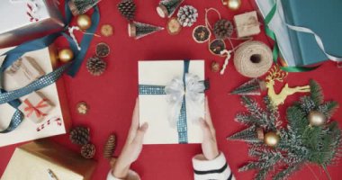 Kırmızı arka planda hediye kutusundan hediye paketini açan kız eli manzarası. Noel kompozisyonu ve yeni yıl tatili sezonunun en az yaratıcı düzlüğü.