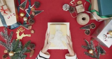 Kırmızı arka planda hediye kutusundan hediye paketini açan kız eli manzarası. Noel kompozisyonu ve yeni yıl tatili sezonunun en az yaratıcı düzlüğü.