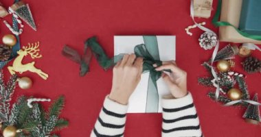 Kırmızı arka planda hediye kutusundan hediye paketini açan kız eli manzarası. Noel kompozisyonu ve yeni yıl tatili sezonunun en az yaratıcı düzlüğü.