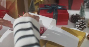 Hediye paketini paketleyen kızların ellerini kapatın. Kış Noel süsleri masanın üzerinde. Geleneksel Noel kompozisyonu ve yeni yıl tatili sezonunun en az yaratıcılığı.