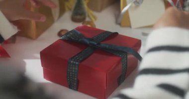 Hediye paketini paketleyen kızların ellerini kapatın. Kış Noel süsleri masanın üzerinde. Geleneksel Noel kompozisyonu ve yeni yıl tatili sezonunun en az yaratıcılığı.