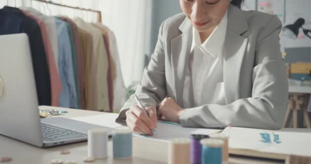 专业快乐的亚洲女商人设计师与笔记本电脑一起坐在桌面上 在工作室工作场所的素描本设计服装时尚新系列 成功的业务 — 图库视频影像