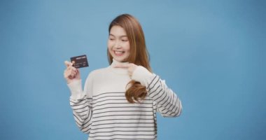 Genç ve çekici Asyalı bayan süveter askısı, ATM ya da banka kartı ya da kredi kartı takıyor ve mavi arka planda izole edilmiş online alışveriş standı için kullanıyor. Kadın başparmakları fotokopi alanı kavramının keyfini çıkarır.