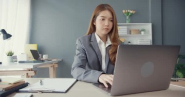 Genç Asyalı iş kadını iş yerindeki ofis masasında çalışırken dizüstü bilgisayar kullanıyor ve iletişim kuruyor. Uzak webinar, internet teknolojisi, yaşam tarzı sosyal uzaklık ve Coronavirüs 'ten sonra çalışma.