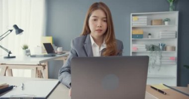 Genç Asyalı iş kadını iş yerindeki ofis masasında çalışırken dizüstü bilgisayar kullanıyor ve iletişim kuruyor. Uzak webinar, internet teknolojisi, yaşam tarzı sosyal uzaklık ve Coronavirüs 'ten sonra çalışma.