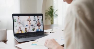 Young asia female listen leader on video call with diverse multiracial colleagues on online with laptop in kitchen at house. Girl student distance learn online at house, Online meeting concept.